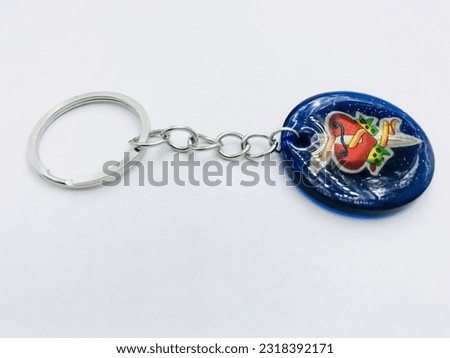 A blue colour, circle shape keytag on white background.It has picture, silver keychain. It made of resin material. This picture was taken from the side of the keytag. Beautiful creative simple keytag.