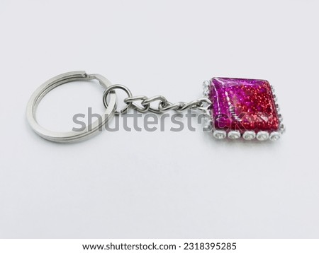 A pink and red colour, square shape keytag on white background.It has glitter powder, silver keychain and border like dots.It made of resin material.This picture was taken from the side of the keytag.
