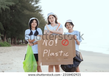 Three volunteer girls holding a no plastic sign on the beach