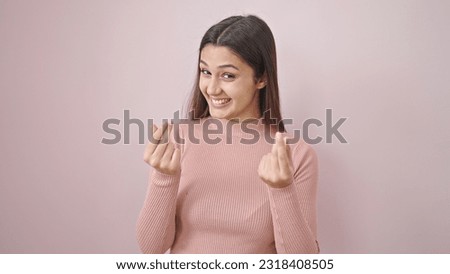 Young beautiful hispanic woman smiling confident doing money gesture over isolated pink background