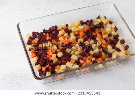 Baked diced vegetables: beets, carrots, potatoes seasoned with spices and vegetable oil in a glass baking dish on a light gray background. Royalty-Free Stock Photo #2318415543