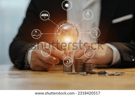 businessman holding a light bulb Concept of saving money with hands putting coins on wooden table floor