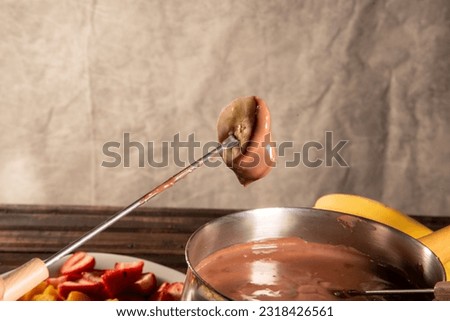 chocolate fondue accompanied by tropical fruits on wooden table and dark background
