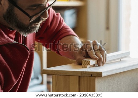 Closeup of a carpenter's hand assembling timber. Man with beard and glasses buiding a piece of forniture in a small bussiness workshop