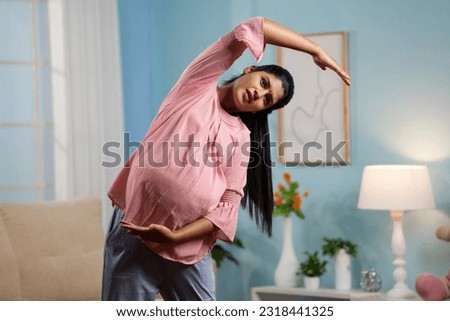 Indian pregnant woman doing stretching exercise or yoga asana at home - concept of healthy lifestyle, maternity workout and relaxation. Royalty-Free Stock Photo #2318441325