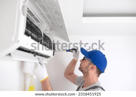Service guy cleaning and maintaining air condition unit. Royalty-Free Stock Photo #2318451925