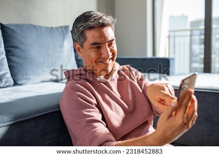 MIddle aged latin man using a smart phone on a couch at home