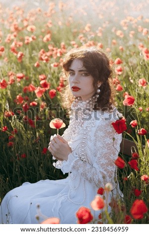 A beautiful girl in a vintage white dress, as a model, at a fashion photo shoot in a poppy field at sunset.