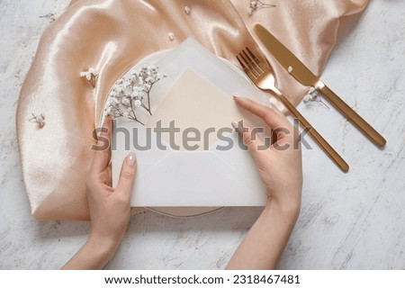 Woman holding envelope with blank invitation card and gypsophila flowers near served table