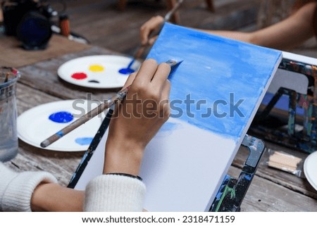 close-up Hand of Asian teenage girl who intended to use a paintbrush to paint on white cloth Draw a picture of the sky. teenage girls love to do things on vacation. to practice drawing skills