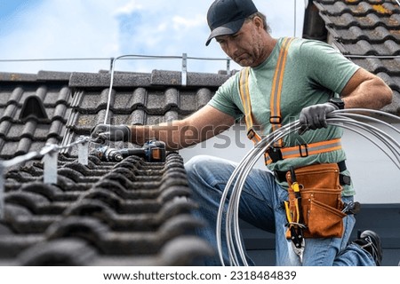 Work on the roof. An electrician installing a lightning rod conductor on a tiles roof.