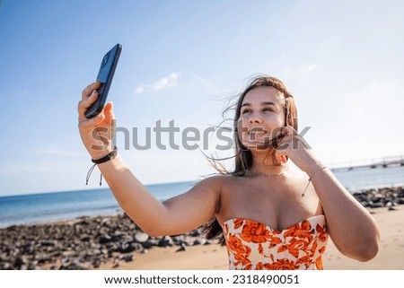 A teenage girl takes a selfie at the beach on a windy day