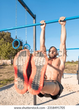 Vertical photo of an athletic young man performing the L-sit exercise at the outdoor calisthenics park - calisthenics concept
