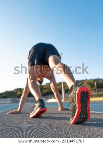 photo detail of young athletic man about to run on the athletics track - sport, training, running concept