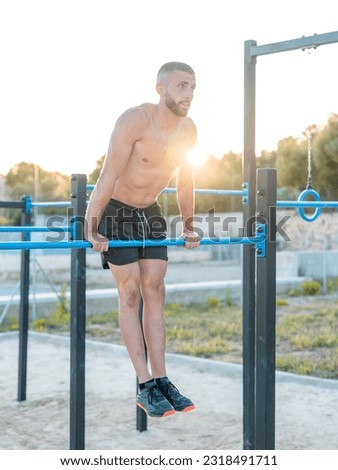 vertical photo of young shirtless athletic man lifting himself over the bar in the calisthenics park at sunset - calisthenics concept