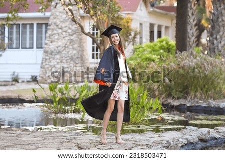 A beautiful young female wearing graduation gown and graduation cap in an outdoor nature setting 
