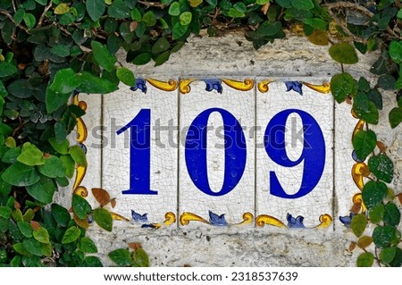 Street sign number 109 on a wall with plants