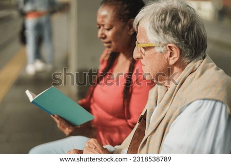 Senior man and african mature woman sitting together at tram station - Elderly nursing care concept Royalty-Free Stock Photo #2318538789