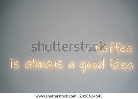 A yellow neon sign on white wall at coffee shop.