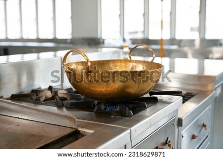 Focus on Brass pan on frame in steel kitchen for cooking food. Royalty-Free Stock Photo #2318629871