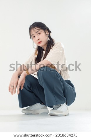 Portrait isolated cutout studio shot of Asian young cute female teenage fashion model with pigtails braids hairstyle in casual trendy wear sitting on floor posing look at camera on white background.