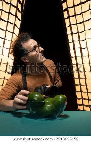 Latin male Photographer wearing glasses checking the flashlights for vegetables Set in a professional Studio. vertical, copy space.	