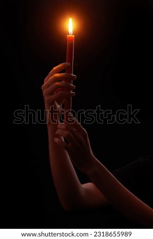 Woman’s hands holding red wax candle burning brightly on black background