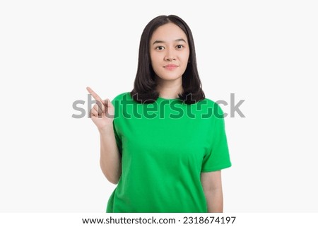 Smiling asian woman pointing finger to the right side with product or empty copy space standing over isolated white background wearing green t-shirt