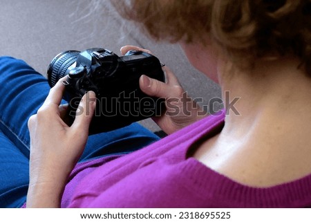 Beautiful photographer woman holding a digital camera sitting in the sofa at home, indoors