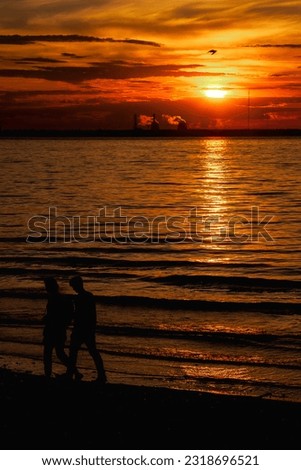 Image of silhouettes man and woman walking at urban beach at city sunset background. View of dusk evening urban landscape for advertising banner. Vitality and city life concept. Copy ad text space