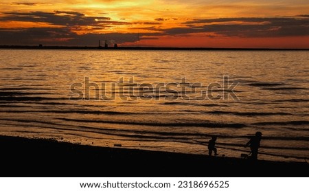 Panoramic view of silhouettes children at urban beach at city orange sunset background. Panorama of evening urban landscape for advertising banner. Vitality and city life concept. Copy ad text space