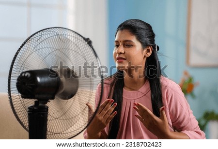 Indian woman using electric fan during hot summer day by sitting in front at home - concept of hot temperature, summertime and relaxation. Royalty-Free Stock Photo #2318702423