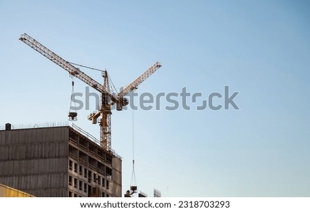 Two industry cranes on creation site house building at blue clean sky. Backdrop of industrial crane on construction site. Construction and renovation of buildings concept. Copy ad text space, poster