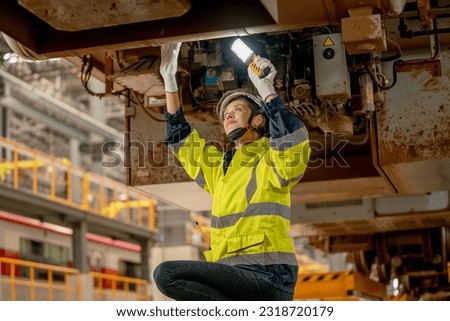 Lower view of train factory or professional technician worker check and fix the problem of the train using hold light stick and stay under electric train in maintenance center. Royalty-Free Stock Photo #2318720179