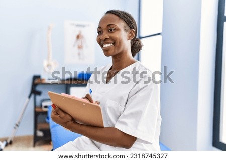 African american woman physiotherapist smiling confident writing medical report at rehab clinic Royalty-Free Stock Photo #2318745327