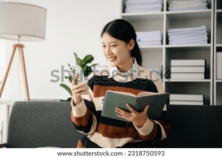Young Asian woman listening music from headphones and writing note for her work idea in diary book.She in home office 
 Royalty-Free Stock Photo #2318750593