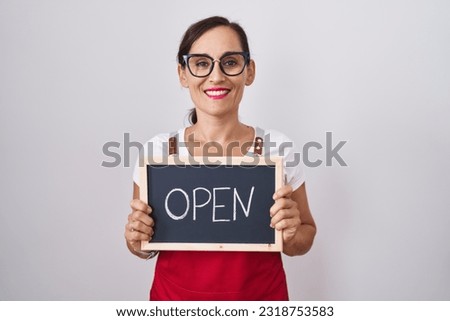 Middle age brunette woman holding banner with open text looking positive and happy standing and smiling with a confident smile showing teeth 