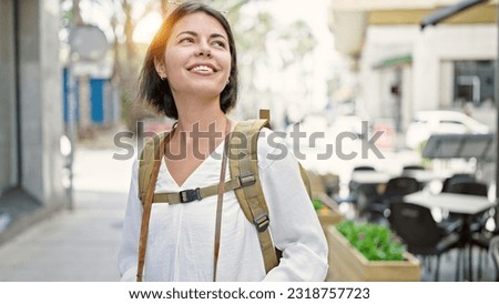 Young beautiful hispanic woman tourist smiling confident wearing backpack at coffee shop terrace