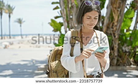 Young beautiful hispanic woman tourist using smartphone at seaside