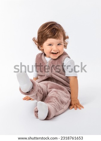 The kid, a 2-year-old toddler, is sitting on the floor in a plush suit, pulling his leg and laughing merrily. Children's gymnastics, exercise. Photo.