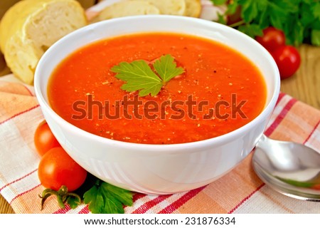 Tomato soup in a white bowl on a napkin, spoon, tomatoes, parsley, bread on a wooden boards background Royalty-Free Stock Photo #231876334