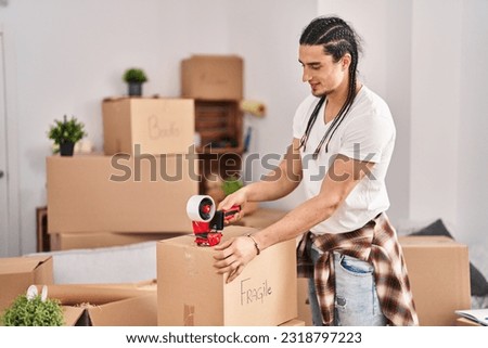 Young man smiling confident packing cardboard box at new home