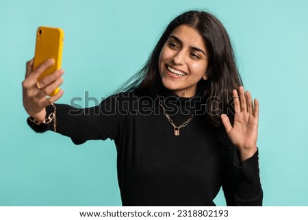 Indian woman traveler blogger, taking selfie on smartphone, communicating video call online with family or friends, live translation stream. Pretty hindu girl isolated on blue background, indoors