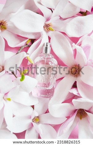 Open bottle of perfume with magnolia flowers, drops of water composition on the pink background. Fresh magnolia aroma. Idea of sweet pure smell of flowers for young girls. Place for text.