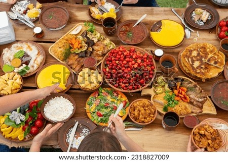 Homemade Romanian Food with grilled meat, polenta and vegetables Platter on camping. 
Top view of group of people having dinner together on wooden table in garden.
