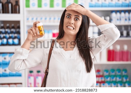 Young brunette woman shopping at pharmacy drugstore holding pills stressed and frustrated with hand on head, surprised and angry face  Royalty-Free Stock Photo #2318828873