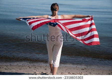Indepence day concept. Woman dressed in white, holds american flag by the ocean.