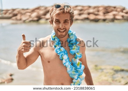 Caucasian man wearing hawaiian lei at the beach smiling happy and positive, thumb up doing excellent and approval sign 