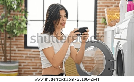 Young caucasian woman washing clothes playing video game at laundry room