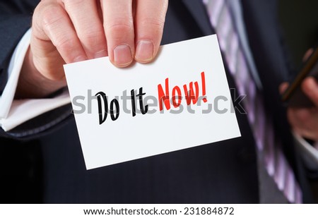 A businessman holding a business card with the words,  Do It Now, written on it.